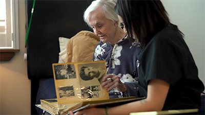 Elderly woman looking at memory album with caregiver