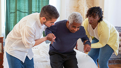 Two caregivers assisting an elderly man stand