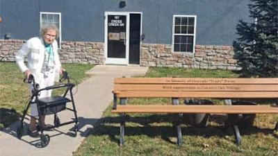 Memory care resident stands with memorial bench